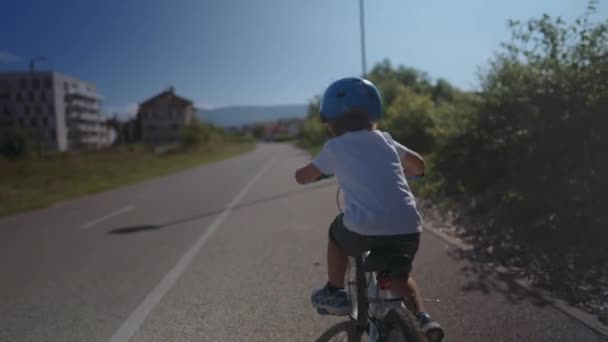 活泼的小男孩骑着自行车在外面绿路上戴着安全帽 — 图库视频影像