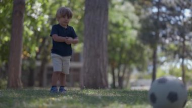 Küçük çocuk dışarıda futbol topunu tekmeliyor.