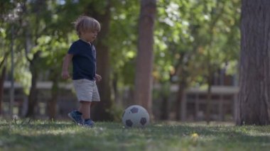 Küçük çocuk dışarıda futbol oynuyor.