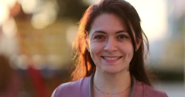 30 'lu yaşlarda bir portre kadın gün ışığında dışarıda kameraya bakıyor.