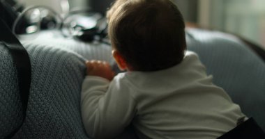 Baby standing by bed, infant learning to stand leaning on bedsheet
