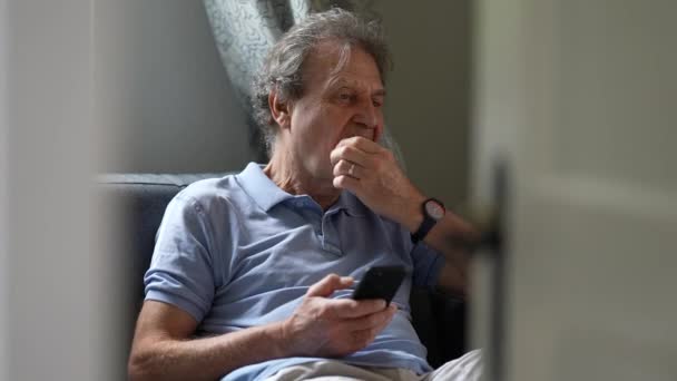 Pensive Senior Man Sitting Sofa Looking Cellphone Device Person Scratching — Video