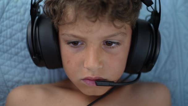 マイク付きのヘッドセットを着てオンラインで若い男の子のゲーム 子供ゲーマー — ストック動画