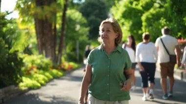 Yeşil şehir şehrinde dışarıda yürüyen yaşlı bir kadın, kıdemli kişi dışarıda yürüyor.