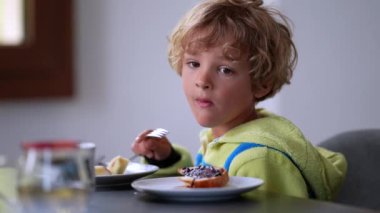 Düşünceli çocuk kahvaltı masasında oturmuş meyve yiyor. Düşünceli çocuk.