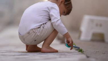 Oyuncak makas oynayan çocuk yeşil bitki yaprağı kesiyor.