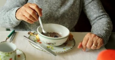 Yaşlı insan sabah kahvaltısında bir kase mısır gevreği ve süt yiyor.