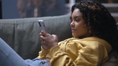 Geceleri koltukta uzanan bir siyah kız cep telefonundan olumsuz mesaj alıyor. Afro-Amerikalı akıllı telefonla şok oldu.