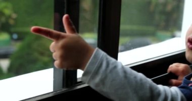 Pencere kenarında duran küçük çocuk, eli ve parmağı ile dışarıyı işaret ediyor.