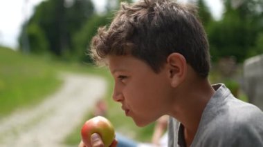 Sağlıklı beslenen çocuk dışarıda elma yiyor.