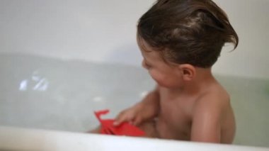 Çocuk oyuncak tekneyle küvette oynuyor.