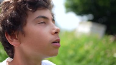 Düşünceli genç bir çocuk dışarıda gözlerini açıyor ve gökyüzüne bakıyor.