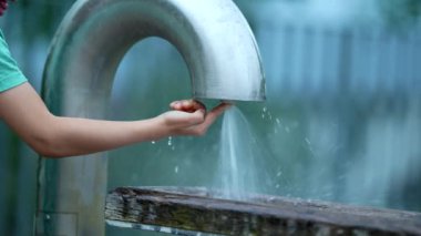 Umumi su musluğuyla oynayan çocuk parmaklarına su sıçratıyor