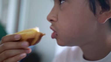 Genç bir çocuk kahvaltıda ballı brioche yiyor. Sabahları karbonhidrat yiyor.