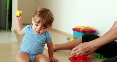 Adorable baby playing with puzzle pieces toys indoors with mom