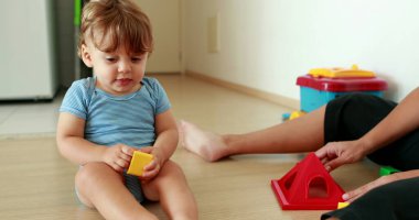 Adorable baby playing with puzzle pieces toys indoors with mom