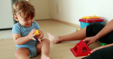 Adorable baby playing with puzzle pieces toys indoors with mom
