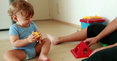 Adorable baby playing with puzzle pieces toys indoors with mom