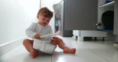 Baby boy hitting metal kitchen utensil on floor. One year old toddler drumming pans and pots