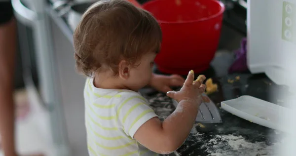 Baby doing a mess at the kitchen, messy one year old infant playing with flour. Toddler child at kitchen cooking
