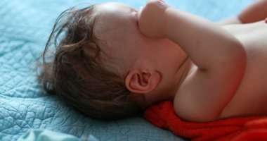 Baby rubbing eyes with hand. Tired one year old infant rubs eye, infant wanting to sleep