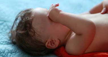 Baby rubbing eyes with hand. Tired one year old infant rubs eye, infant wanting to sleep