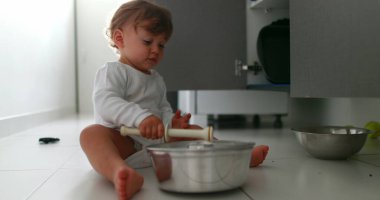 Baby playing with pans and pots on kitchen floor. One year old toddler infant hitting metal utensil