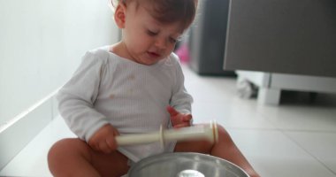 Baby on floor playing with kitchen utensils. One year old toddler drumming and hitting metal utensil