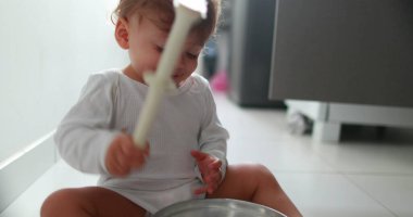 Baby on floor playing with kitchen utensils. One year old toddler drumming and hitting metal utensil