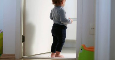 Baby standing by home bathroom, one year toddler stands observing