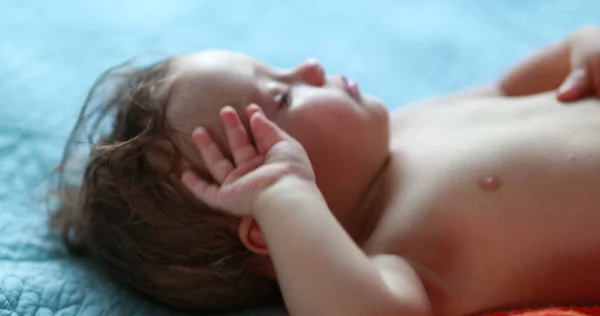 Baby rubbing eyes with hand. Tired one year old infant rubs eye, infant wanting to sleep