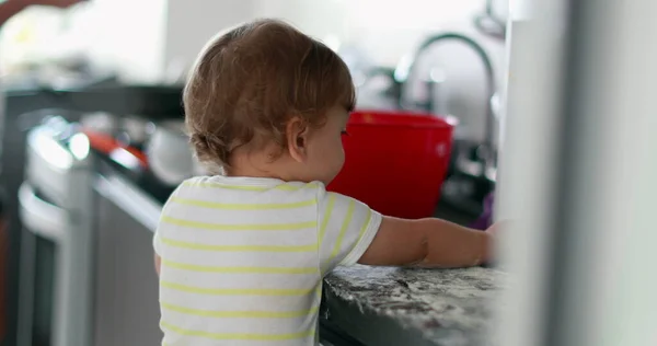 Baby playing covered with flour at kitchen, infant doing a mess with dough cooking