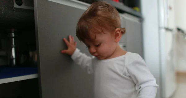 Baby stepping on kitchen floor and closing cabinet cupboard. one year old toddler standing at kitchen