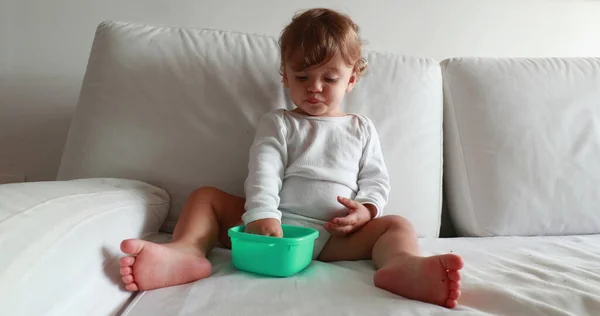 Calm cute baby sitting on couch eating snack