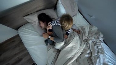 Mother and child in bed in the morning. kid jumping on top of parent lying in bed