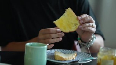 Kadın kahvaltıda ekmeğe bal jölesi sürüyor.