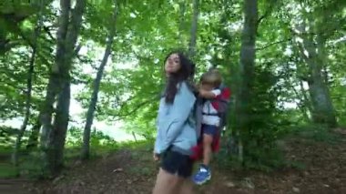 Anne sırt çantasındaki çocukla yürüyüşe çıkıyor anne çocuğu sırtında taşıyor.