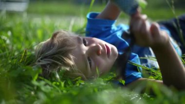 Child lies on grass playing and daydreaming
