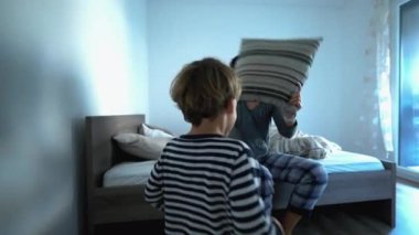 Playful mother and child playing with pillow fight in morning bed, authentic real life family play