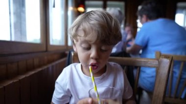 Lokantada saman kullanarak içecek içen küçük çocuk.