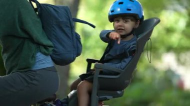 Bisikletli çocuk arka koltukta, ailesi dışarıda kask takıyor.