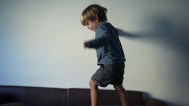 Mutlu küçük çocuk kanepede zıplayıp oynuyor.