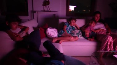 Çocuklar ve anneleri gece televizyon izliyorlar.