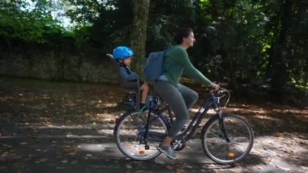 妈妈在公园外面骑自行车 孩子坐在后座上 — 图库视频影像