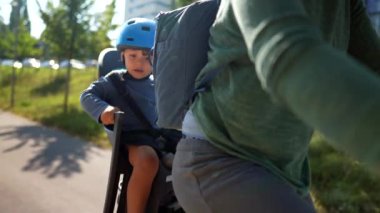 Bisikletin arka koltuğundaki çocuk, anne çocuğuyla arka koltukta kask takıyor.