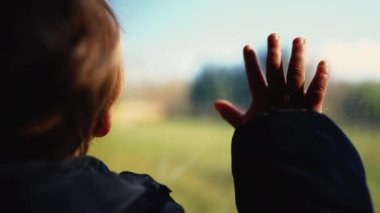 Çocuk elleri trenin camında gezen manzarayı görüyor.