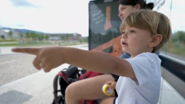 Çocuk ve anne otobüs durağında bekliyor. Çocuk ufku işaret ediyor.