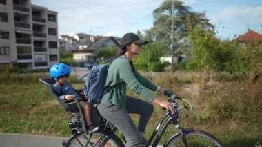 Arka koltukta çocukla bisiklete binen anne şehir yeşili yolda.