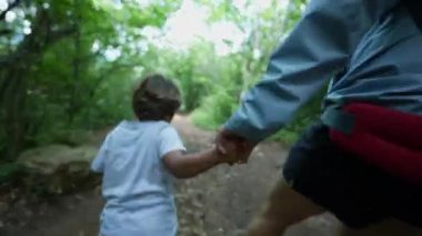 Ebeveyn ve çocuk doğa yürüyüşü yaparken anne elini tutuyor.