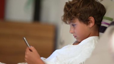 Samimi bir çocuk elinde telefonla cep telefonu ekranına bakıyor.